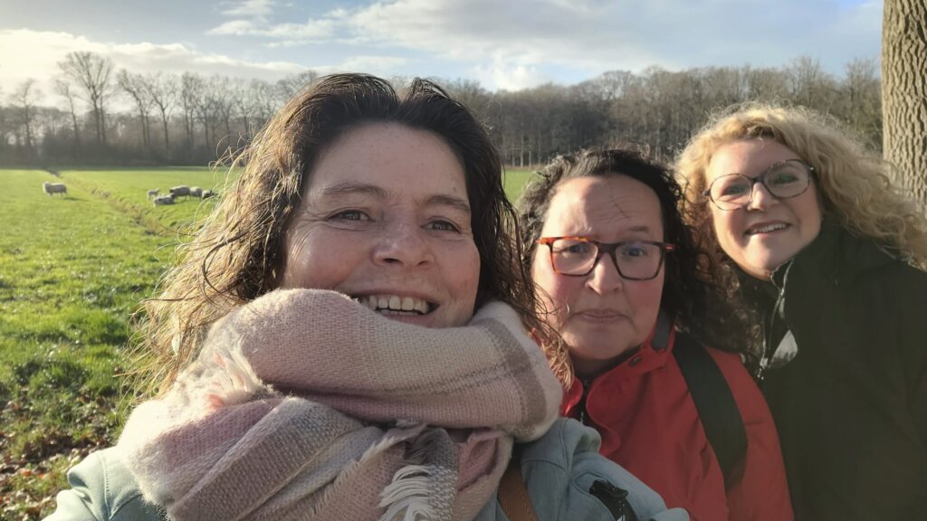 Drie vrouwen maken een selfie in een groene omgeving met schapen op de achtergrond.