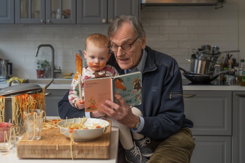 Een man leest een boek voor aan een peuter met spaghetti-vlekken.
