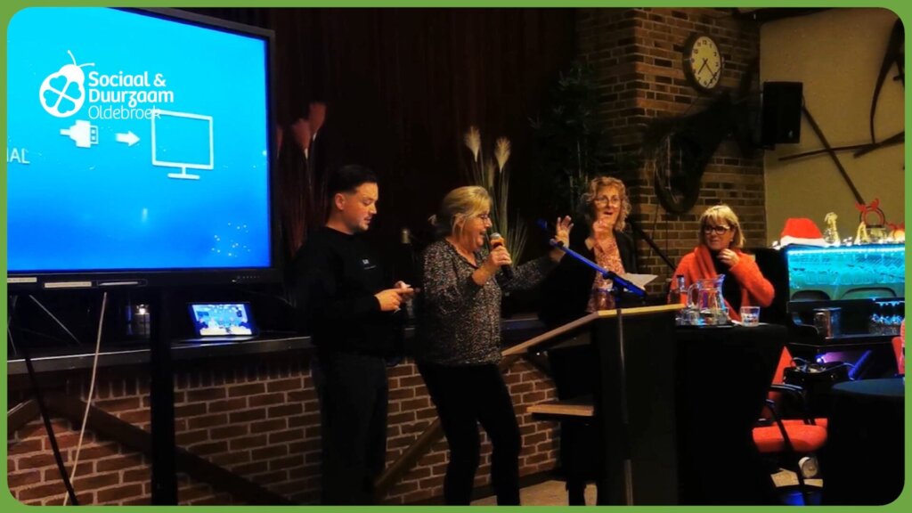 Mensen staan aan een podium voor een grote blauwe presentatiescherm met logo Sociaal & Duurzaam Oldebroek.
