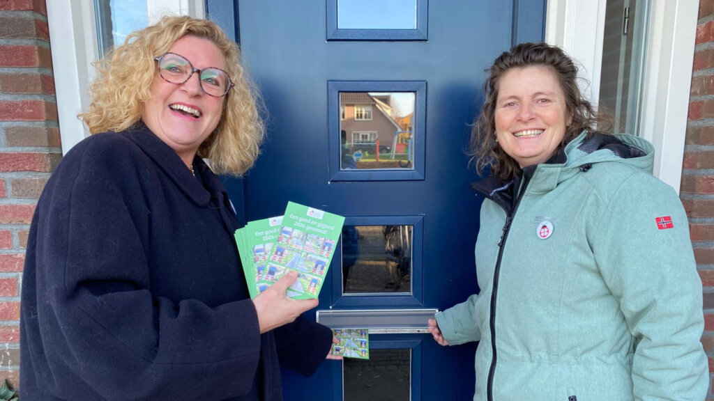 Twee vrouwen staan bij een blauwe deur met folders in hun handen.
