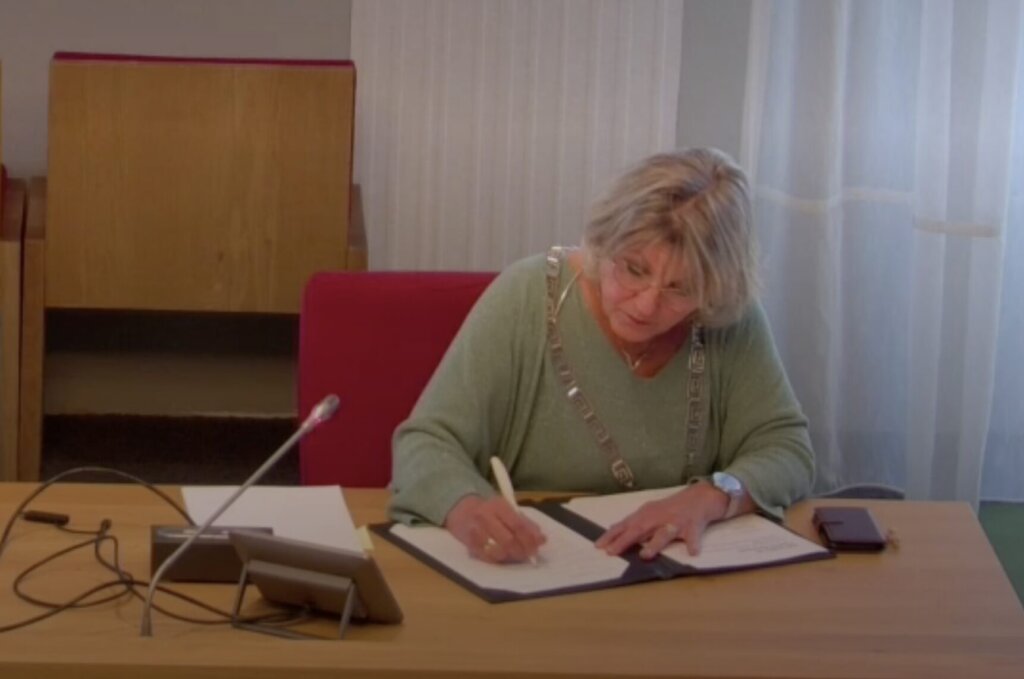 Een vrouw schrijft in een boek op een tafel met een tablet en een smartphone.