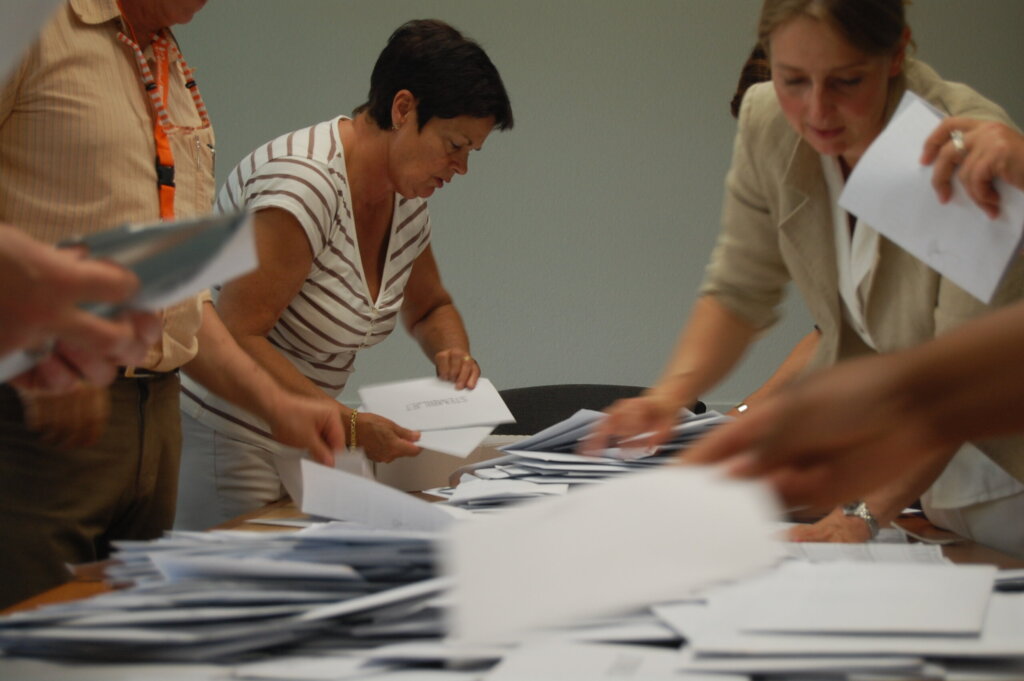 Mensen sorteren stapels papieren aan een tafel.